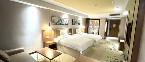 A hotel room with a bed, a desk, a chair, a nightstand, and a wall-mounted lamp.
