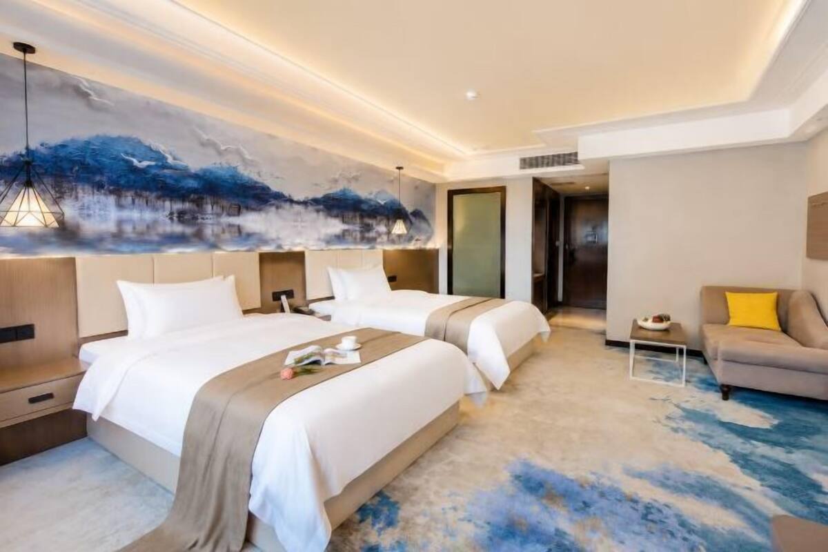 Une chambre d’hôtel avec deux lits, un canapé, un tableau et une moquette.