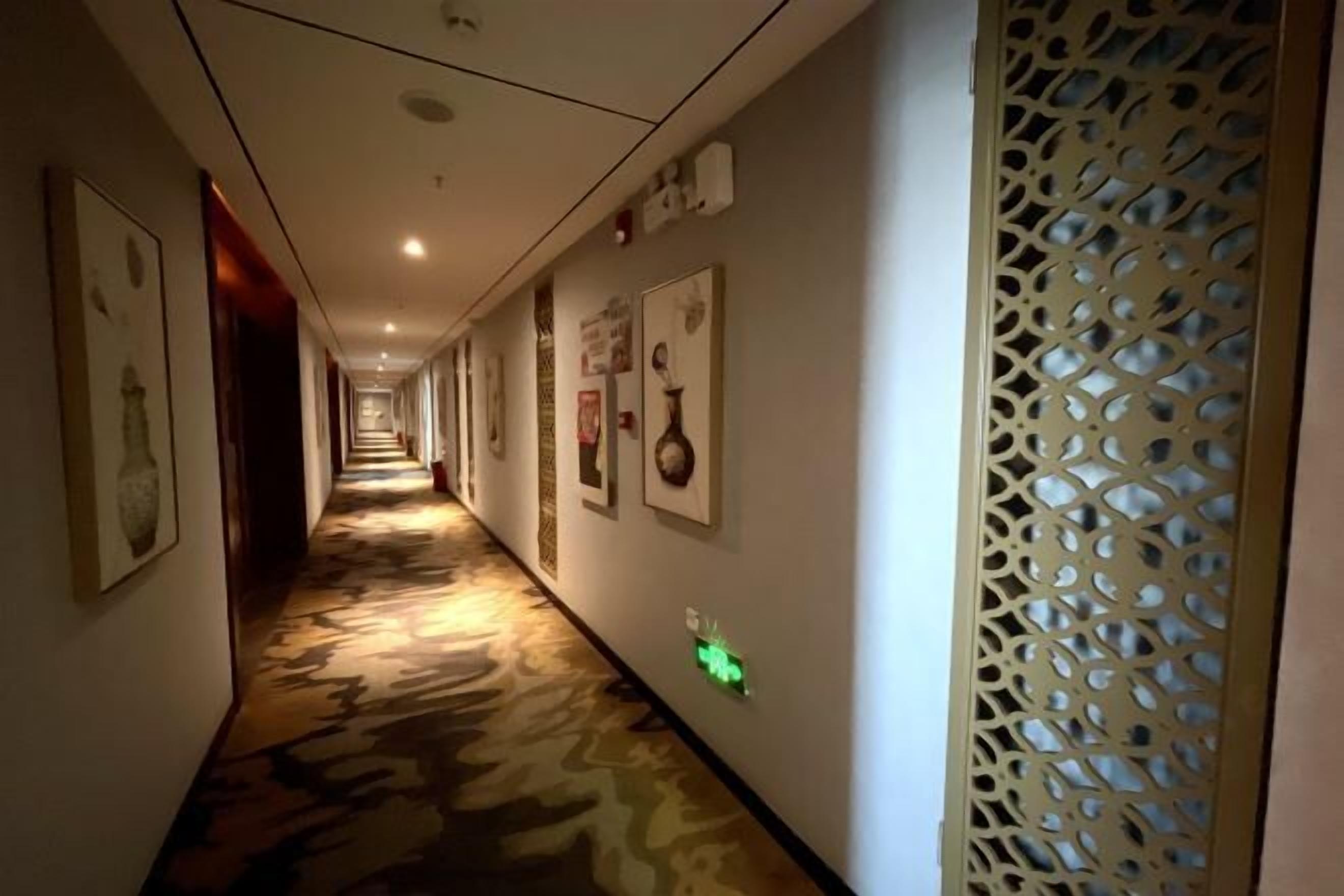 En hotellkorridor med ett mönstrat golv, inramade konstverk på väggarna och en dekorativ skärm på höger sida.
