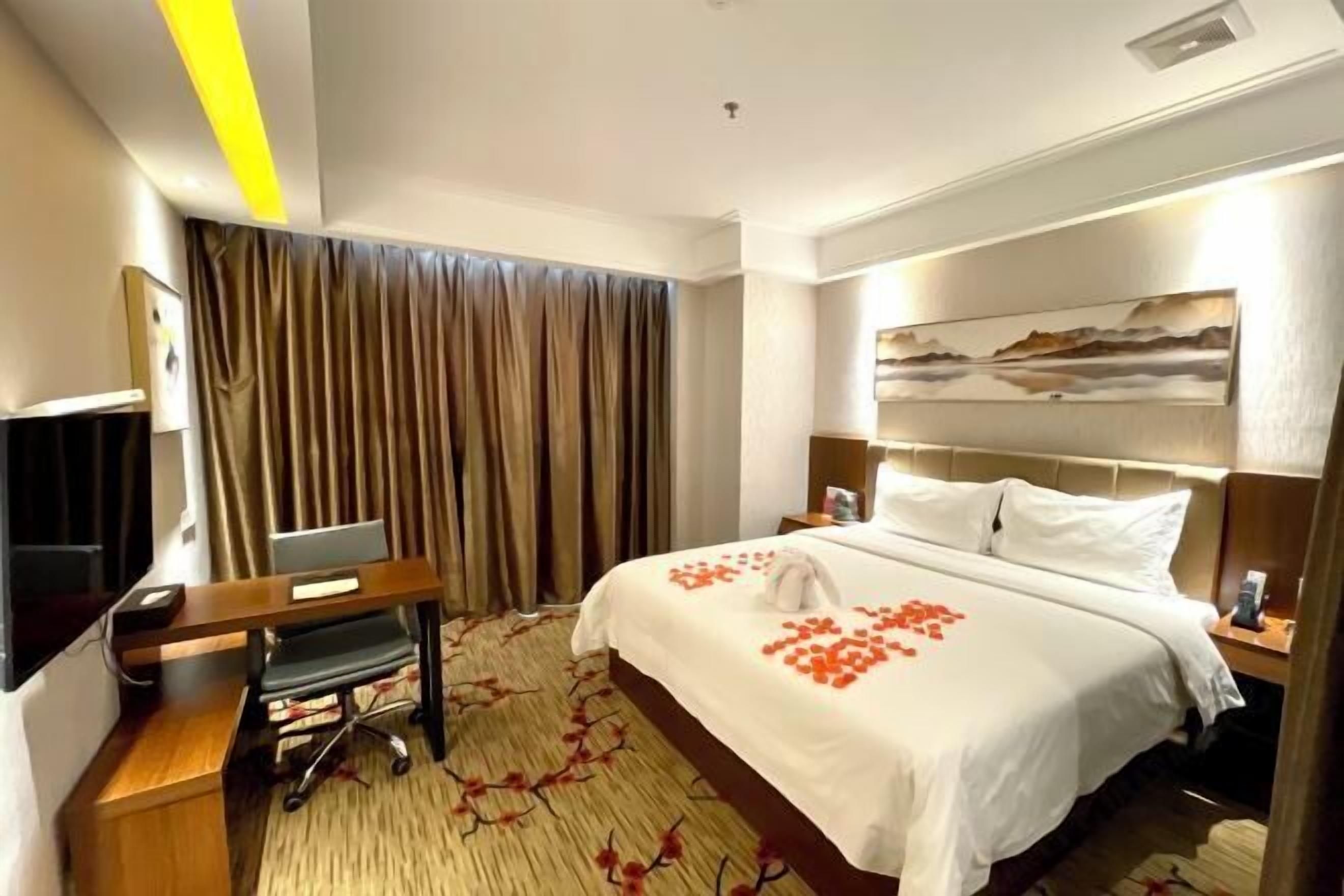 A hotel room with a bed, a desk with a computer, a TV, and a painting on the wall.