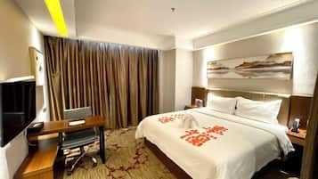 A hotel room with a bed, a desk with a computer, a TV, and a painting on the wall.