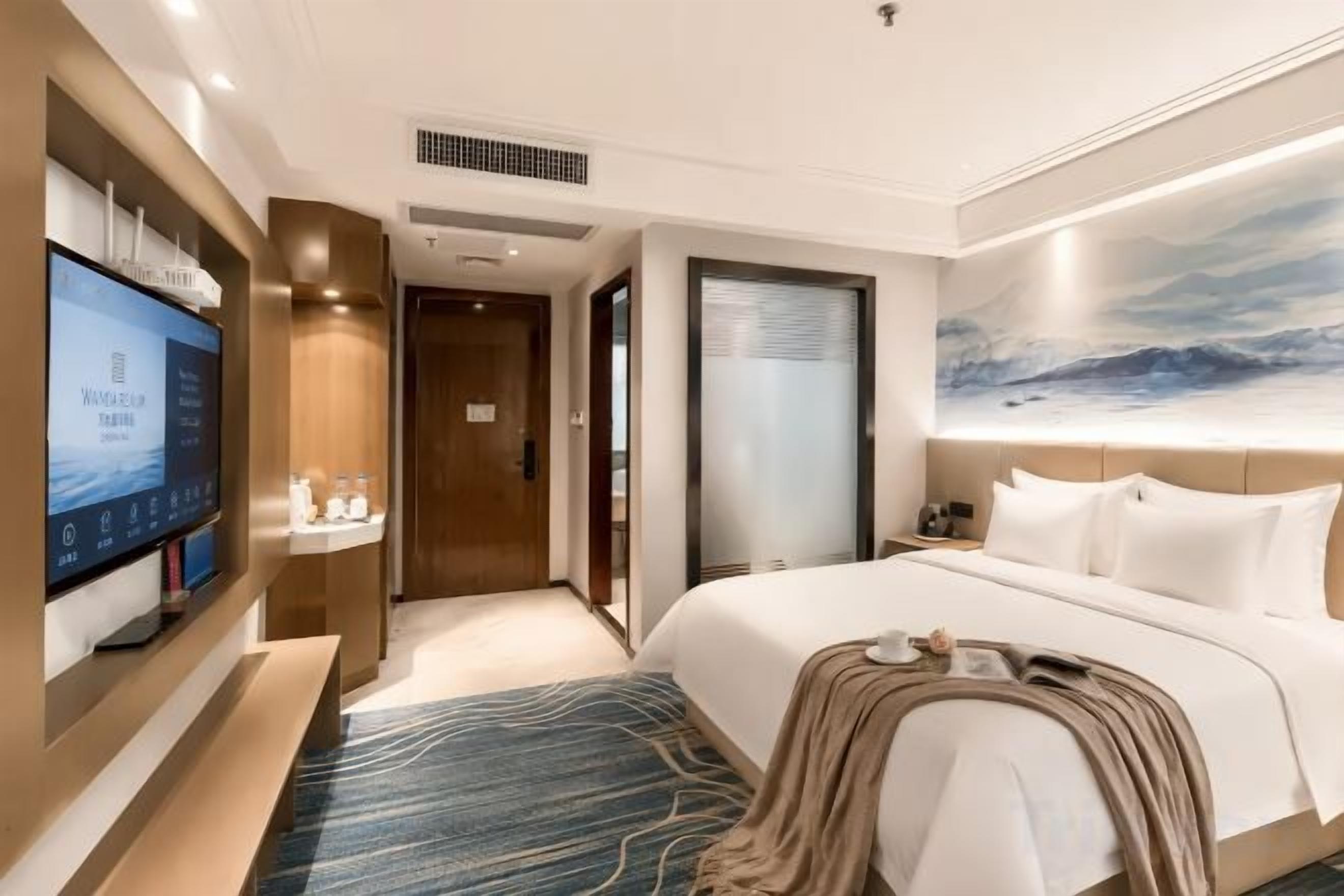 A hotel room with a bed, a TV, a desk, and a bathroom door.
