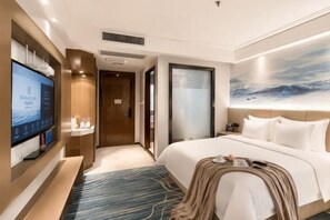 A hotel room with a bed, a TV, a desk, and a bathroom door. - Jinxiu Xiangjiang Hotel (Foshan Jinsha) (Foshan)