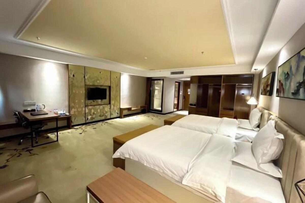 A hotel room with a large bed, a desk with a chair, a TV, and a wardrobe.