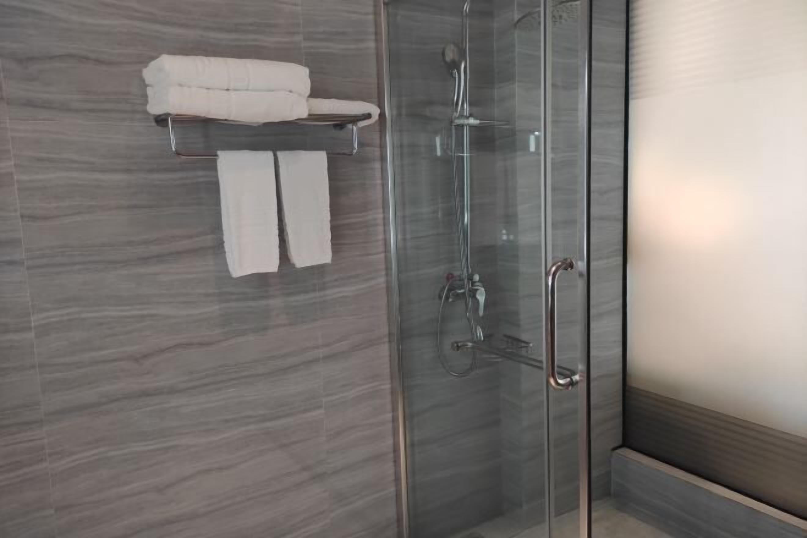 Ett modernt badrum med en duschavdelning med glasväggar, en handduksställning med två handdukar och en vägg beklädd med marmor.