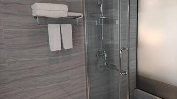 Ett modernt badrum med en duschavdelning med glasväggar, en handduksställning med två handdukar och en vägg beklädd med marmor.