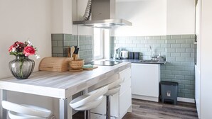 A modern kitchen with a marble countertop, a built-in stove, and a green-tiled backsplash. - Albatros aan Zee - Zandvoort (Zandvoort)