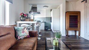 A modern kitchen with a central island, a dining area with bar stools, a wooden cabinet, and a brown leather sofa. - Albatros aan Zee - Zandvoort (Zandvoort)