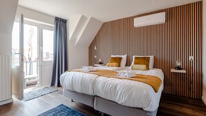 A modern hotel room with a large bed, a wooden slatted wall, a ceiling fan, and a view through a glass door. - Albatros aan Zee - Zandvoort (Zandvoort)