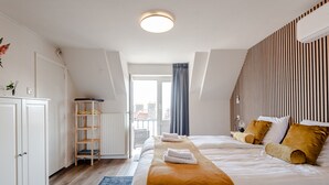 A modern hotel room with a large bed, a wooden wardrobe, a small shelf, a radiator, and a view of the city through a window. - Albatros aan Zee - Zandvoort (Zandvoort)
