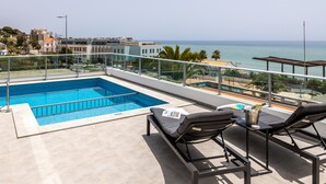 Ein Poolbereich auf dem Dach mit freiem Blick auf den Ozean, Liegestühlen und einer gefliesten Terrasse.