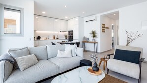 Ein modernes Wohnzimmer mit einem grauen Sofa, einem weißen Sessel und einem Couchtisch aus Marmor.