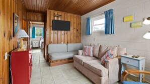 Ein gemütliches Zimmer mit Holzwänden, einem grauen Sofa, einer roten Kommode und einem kleinen Tisch mit Lampe.