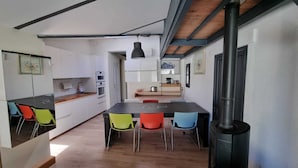 Una cocina moderna con una isla central, sillas coloridas y una estufa de leña.