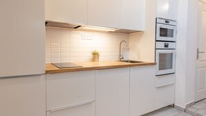 Una cocina moderna con armarios blancos, encimera de madera, horno empotrado y una pequeña planta en maceta.