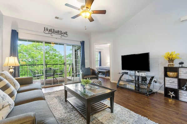 A living room with a sofa, coffee table, TV, and a balcony with a view. - Holiday Ridge Retreat Duo - Holiday Hills Branson - Golf Resort - Outdoor Pools (Branson)