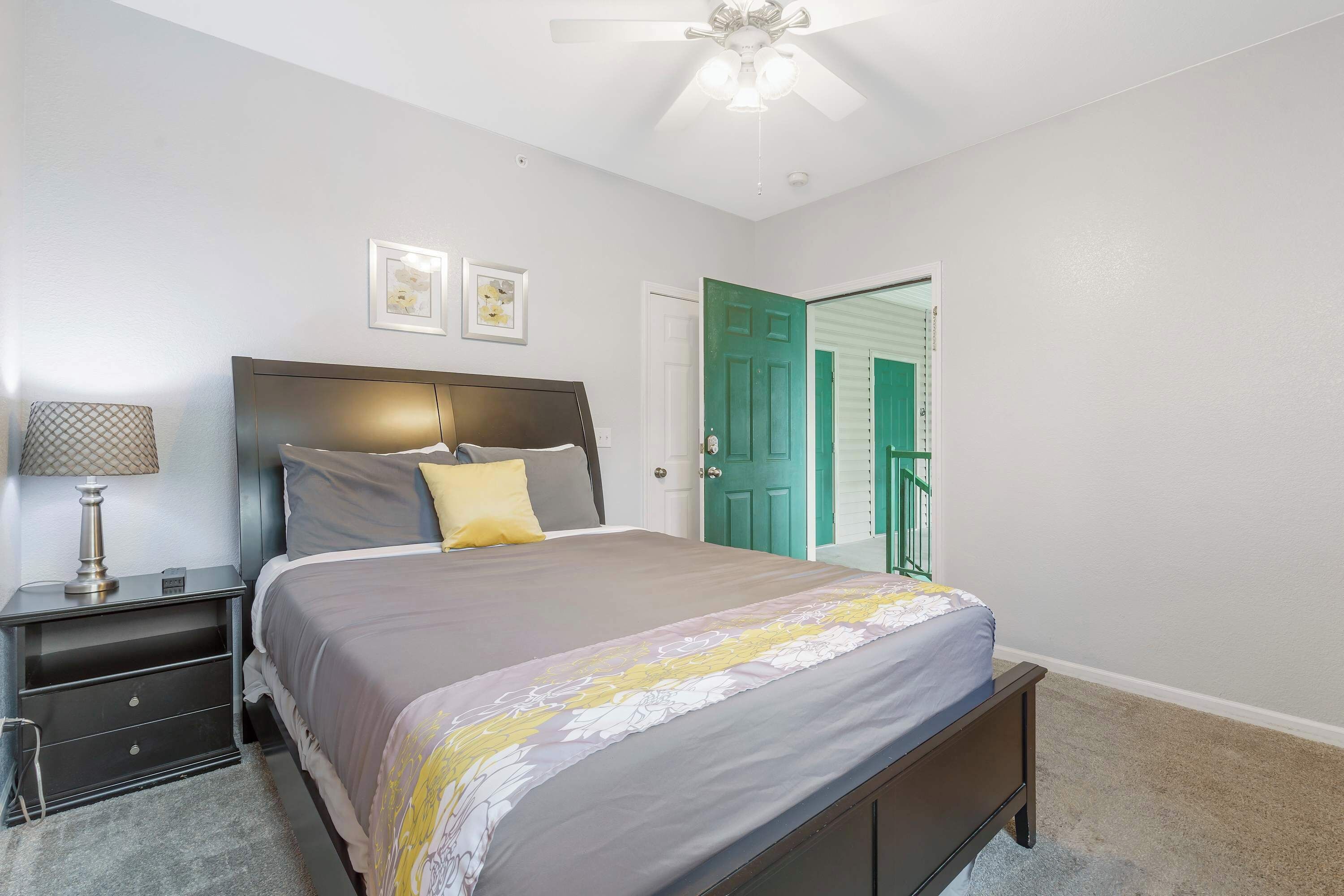 A bedroom with a bed, nightstand, lamp, ceiling fan, and a door with a green frame.
