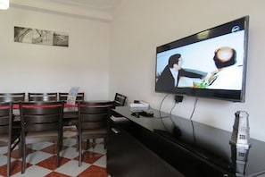 A hotel reception area with a flat-screen TV displaying a scene, a reception desk, and several chairs.