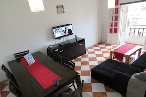 A room with a dining table, a black sofa, a TV on a stand, and a checkered floor.
