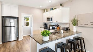 A modern kitchen with white cabinets, stainless steel appliances, a granite countertop, and a small island with bar stools. - Our Happy Place in the Heart of Branson (Branson)