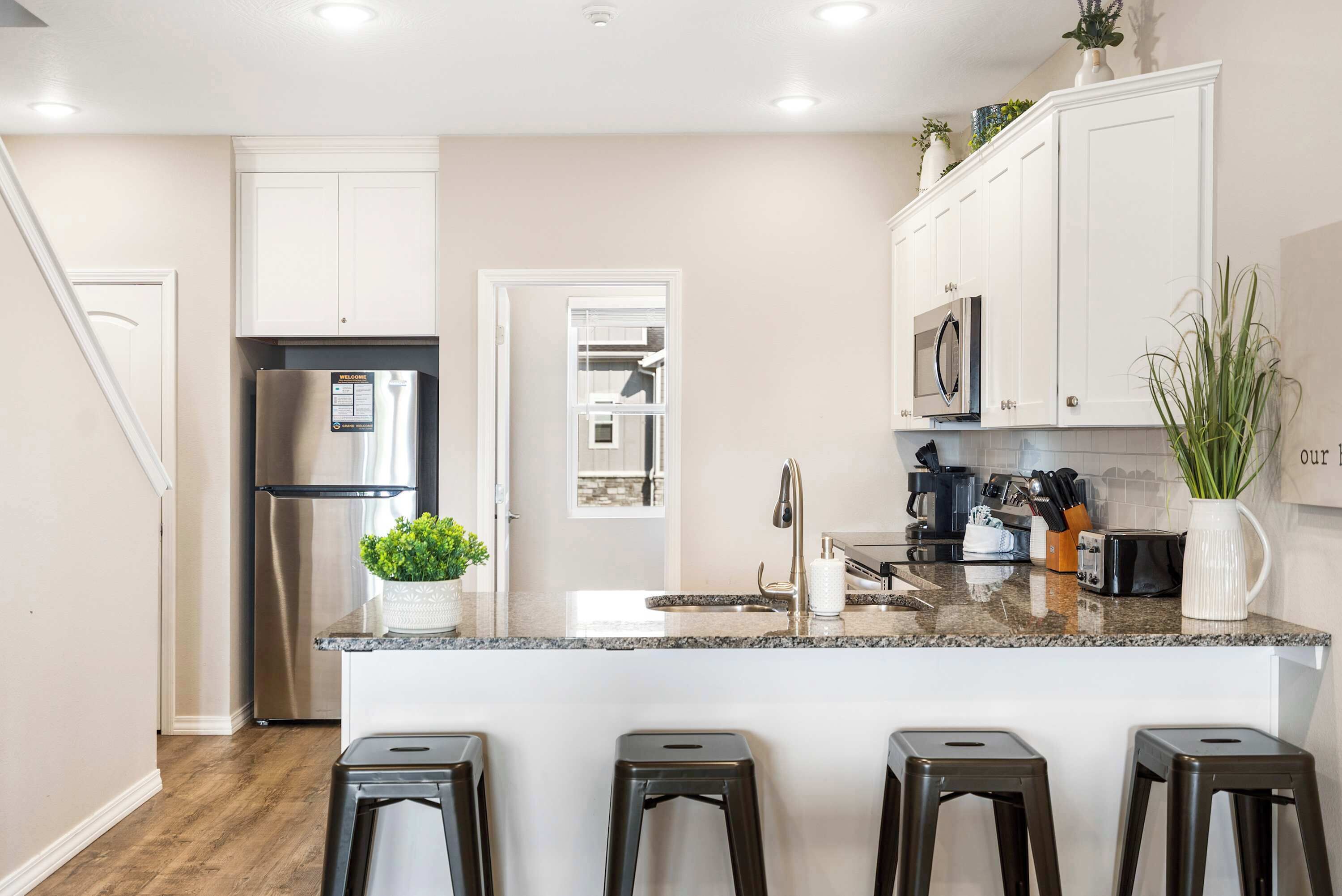 Una cocina moderna con armarios blancos, un refrigerador de acero inoxidable, una encimera de granito y una pequeña isla con taburetes de bar.
