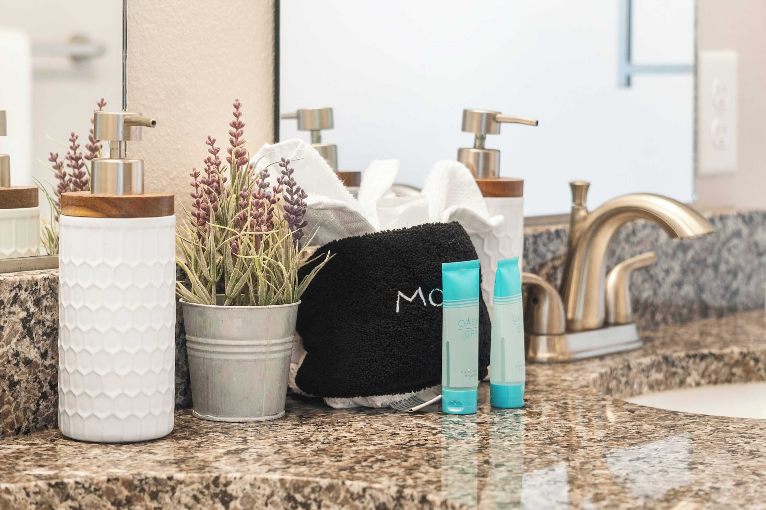 A bathroom counter with a white textured container, a potted plant, a black towel, and two blue toiletry bottles.