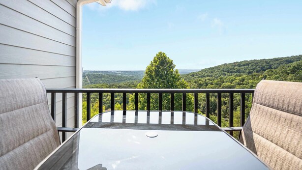 A balcony with a table and chairs, overlooking a forested landscape. - Our Happy Place in the Heart of Branson (Branson)