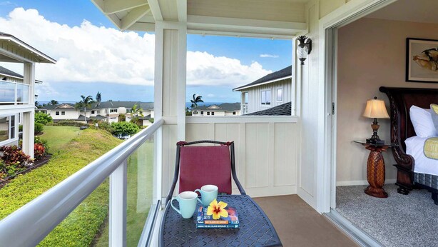 A balcony with a view of a residential area, a chair, a table with books and a flower, and a lamp. - Na Hale O Keauhou Beach Views, Hot Tub & Pool (Kailua-Kona)