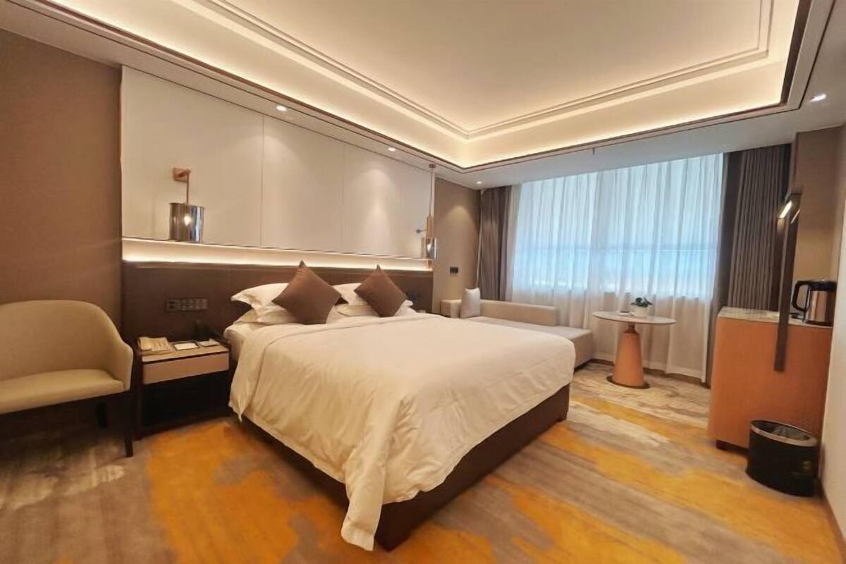 Una habitación de hotel moderna con una cama grande, mesitas de noche, un escritorio y un ventanal con cortinas.