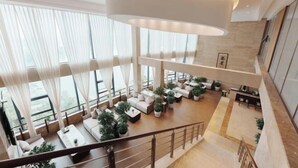 Amplia sala de estar de varios niveles con un diseño moderno, que incluye un gran espacio central con sofás y una mesa de centro, rodeado de plantas en macetas.
