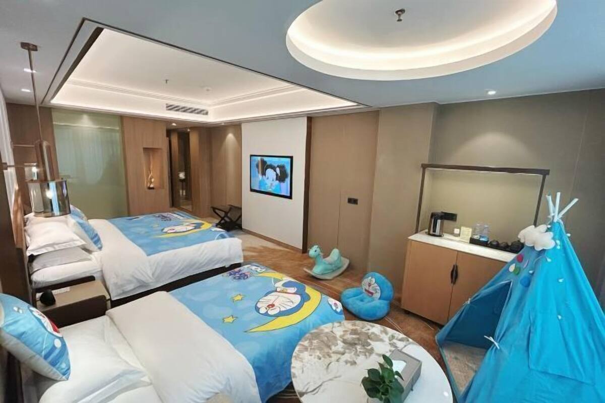 Habitación de hotel con dos camas, un escritorio, una silla, un televisor, un armario y una estructura similar a una tienda de campaña.
