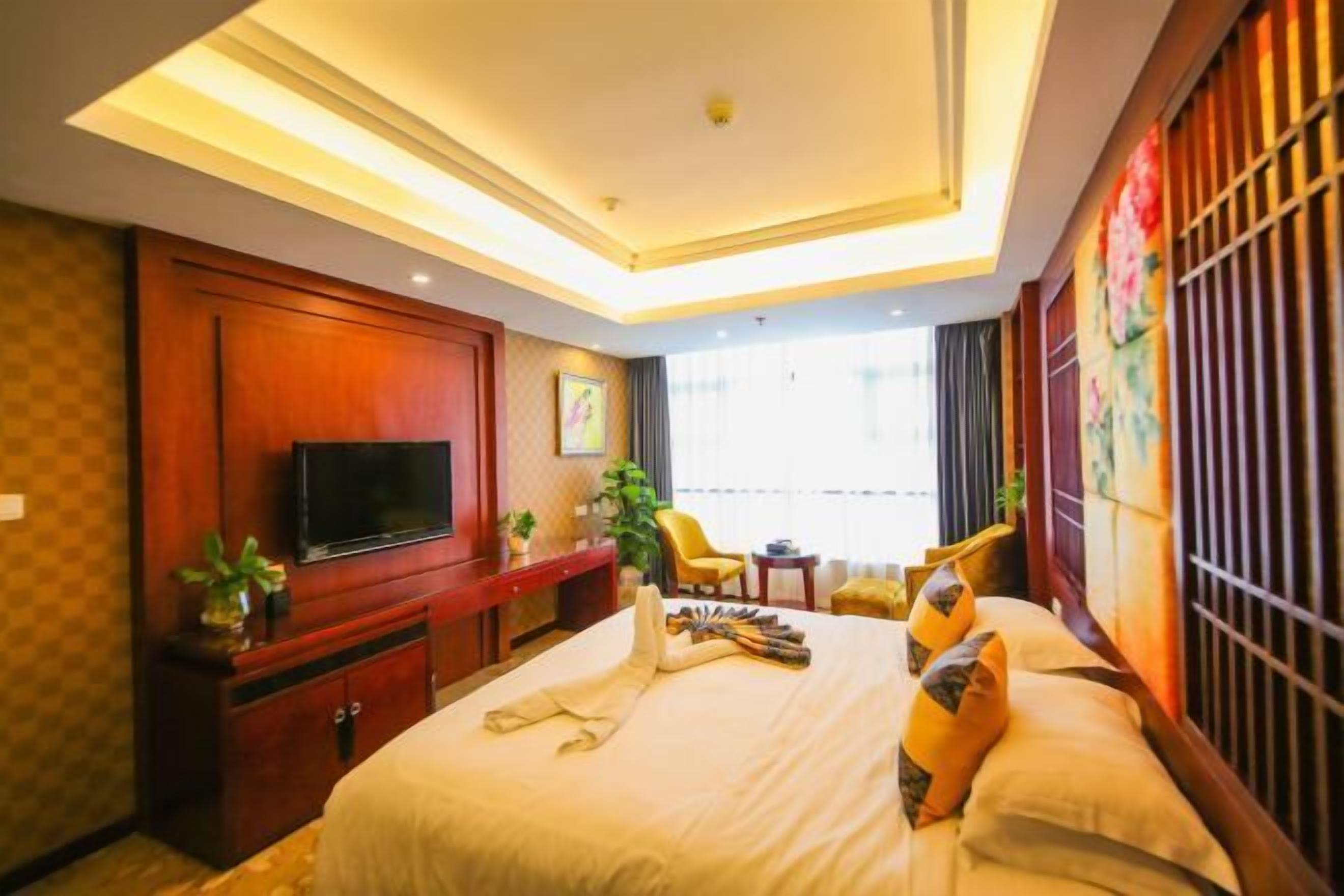 Habitación de hotel con cama, televisión, escritorio y ventana con cortinas.