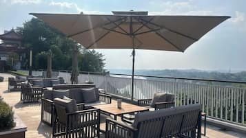 An outdoor seating area with tables and chairs, a large umbrella, and a view of a distant landscape.