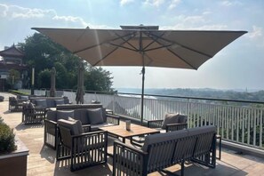 An outdoor seating area with tables and chairs, a large umbrella, and a view of a distant landscape. - Antai Yinshan Jinjiang Hotel (Wusheng)