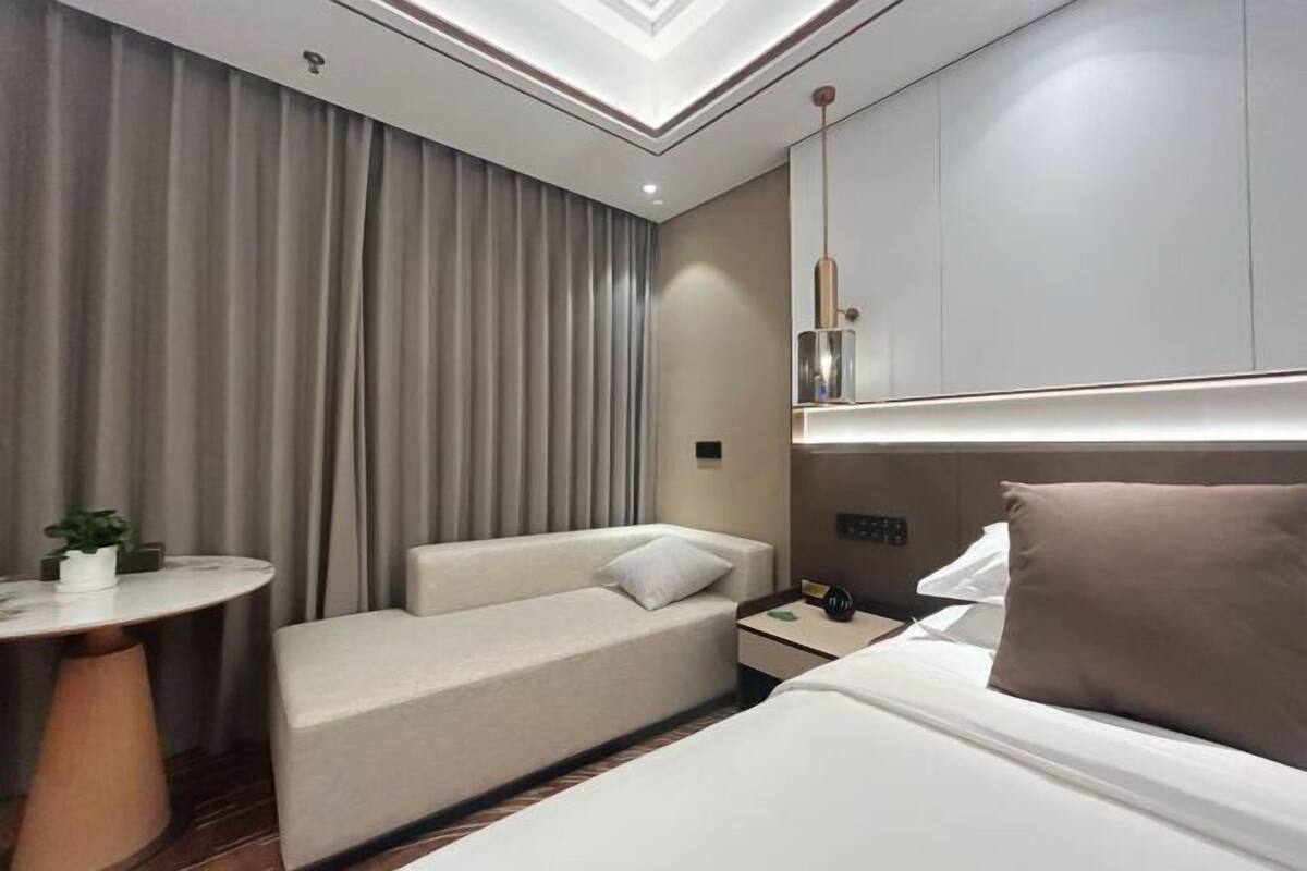 Una habitación de hotel moderna con una cama, un sofá, una pequeña mesa redonda y una mesita de noche.