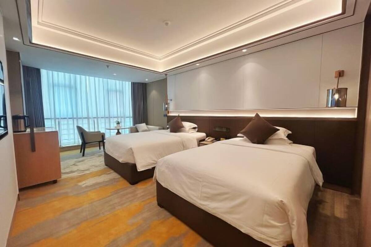Una habitación de hotel con dos camas, un escritorio, una silla y un ventanal grande.