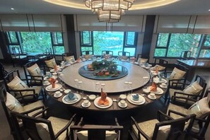 A round dining table with chairs, surrounded by windows, and a chandelier. - Antai Yinshan Jinjiang Hotel (Wusheng)