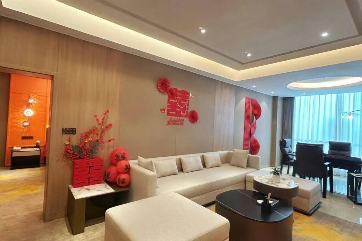 Una sala moderna con sofá, reposapiés y mesa de centro, un piano y detalles decorativos en rojo.