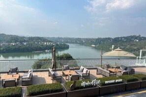 A terrace with outdoor seating overlooking a river, a covered area, and a view of a cityscape. - Antai Yinshan Jinjiang Hotel (Wusheng)
