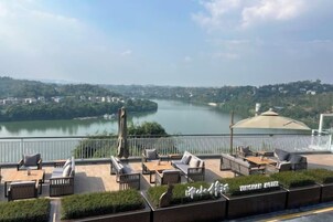 Terraza con mobiliario exterior que da a un río, una zona cubierta y vistas panorámicas de un paisaje urbano.