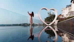 Una persona de pie sobre una superficie reflectante con una estructura en forma de corazón al fondo.