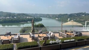 Una terraza en la azotea con mobiliario exterior, vistas de un río y un paisaje urbano distante.