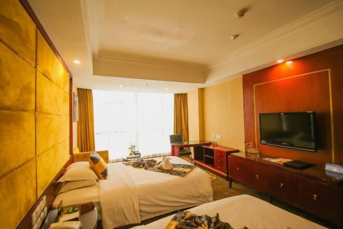 Una habitación de hotel con dos camas, televisión, escritorio y un amplio ventanal.