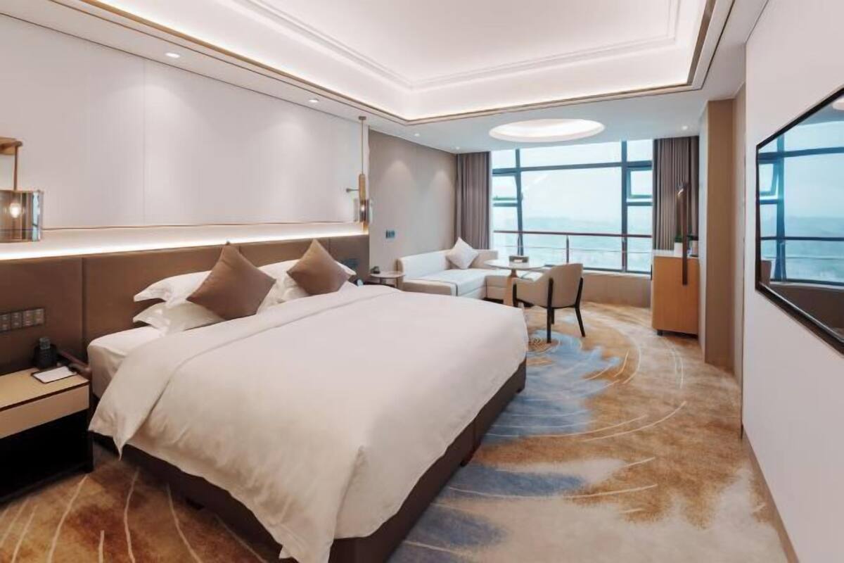 Una habitación de hotel moderna con una cama grande, mesitas de noche, un escritorio y vista al mar.