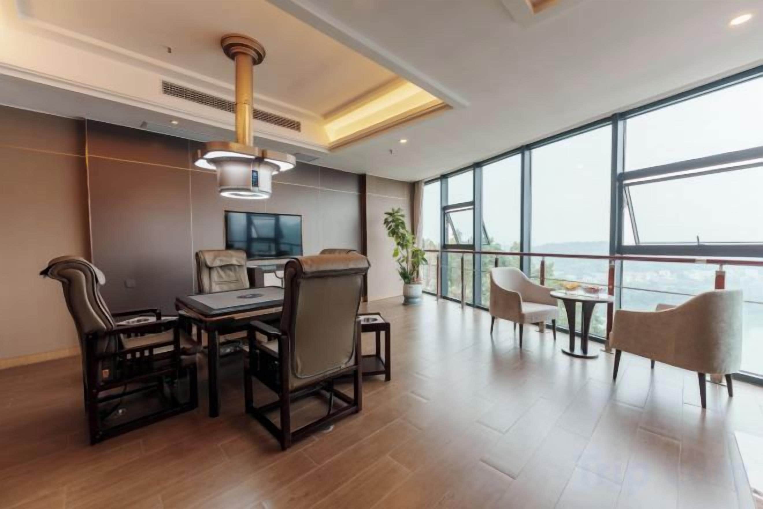 A modern hotel room with a large window, a dining area with a table and chairs, and a seating area with sofas.