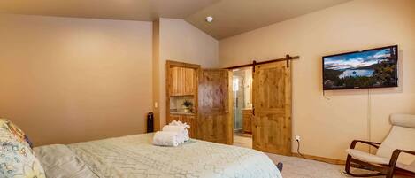A bedroom with a bed, a chair, a painting, and wooden doors leading to another room.