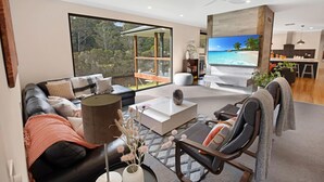 A modern living room with a large TV, comfortable seating, and a view of the outdoors. - Rivers Edge: Experience a truly unique and serene holiday (Toorloo Arm)