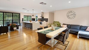 A modern open-plan living and dining area with a kitchen, wooden flooring, and large windows. - Rivers Edge: Experience a truly unique and serene holiday (Toorloo Arm)