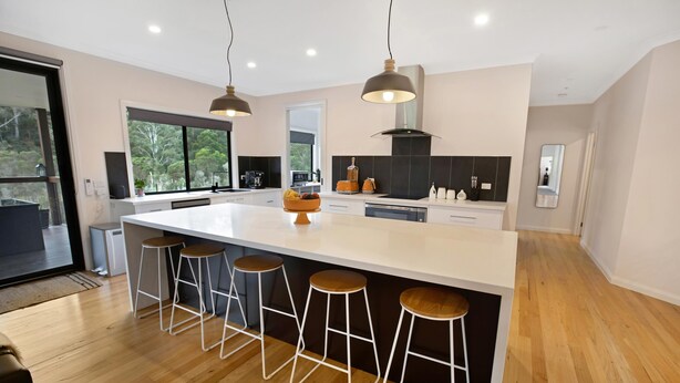 A modern kitchen with a large island, bar stools, pendant lighting, and a view of the outdoors. - Rivers Edge: Experience a truly unique and serene holiday (Toorloo Arm)