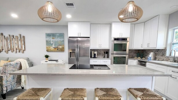 A modern kitchen with white cabinets, stainless steel appliances, and a central island with bar stools. - Hello Sunshine! 4 Bedroom w/Pool and Outdoor Bar (Tampa)